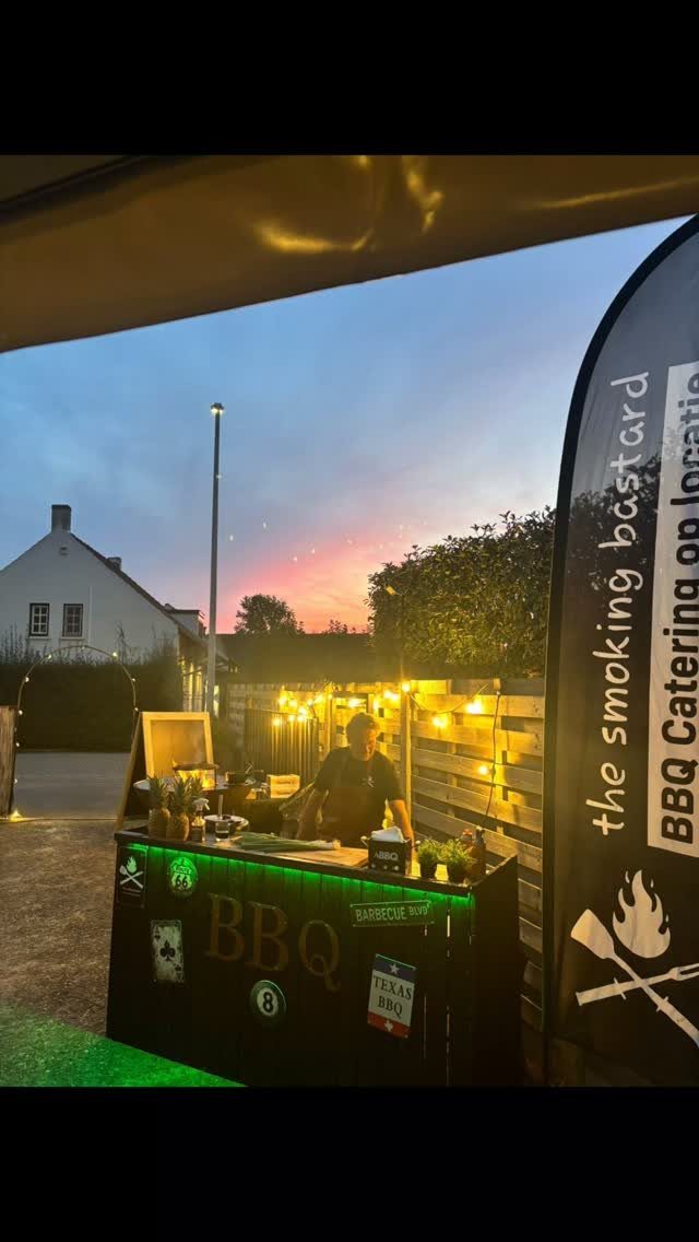 A person working behind a decorated BBQ catering bar in a backyard at sunset.