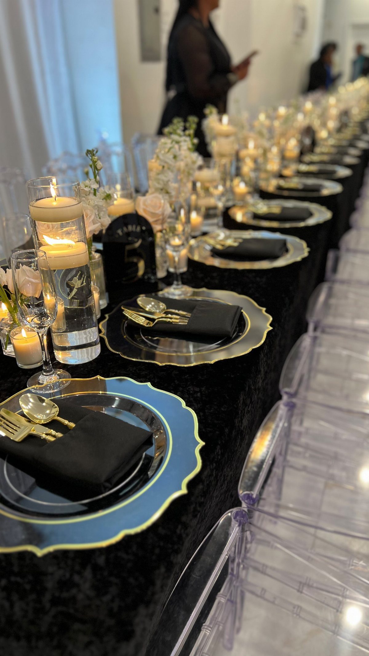 A long formal dining table decorated with black and gold tableware and lit candles.