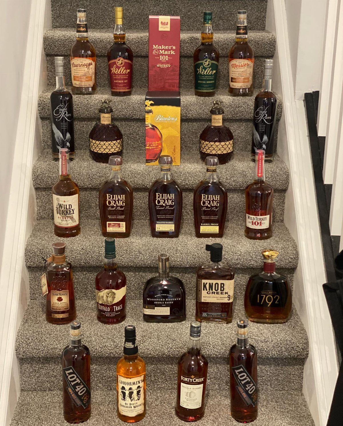 Numerous bourbon bottles arranged neatly on the steps of a carpeted staircase.