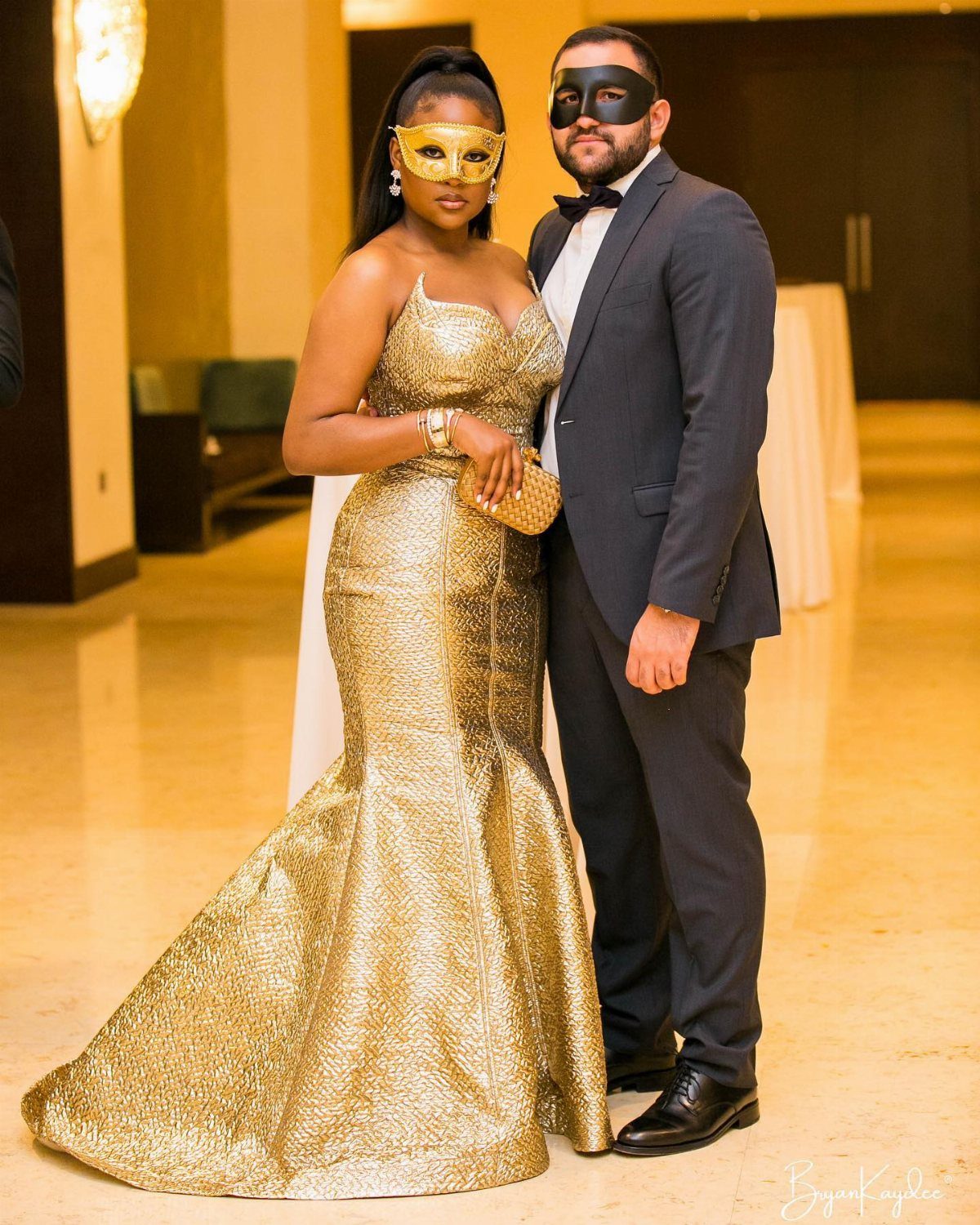A man in a suit and a woman in a gold gown wearing masquerade masks.