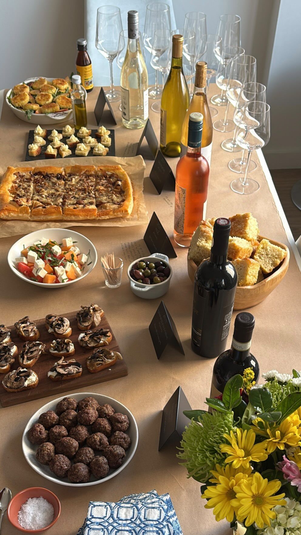 A long table spread with various appetizers, wine bottles, and many empty wine glasses.