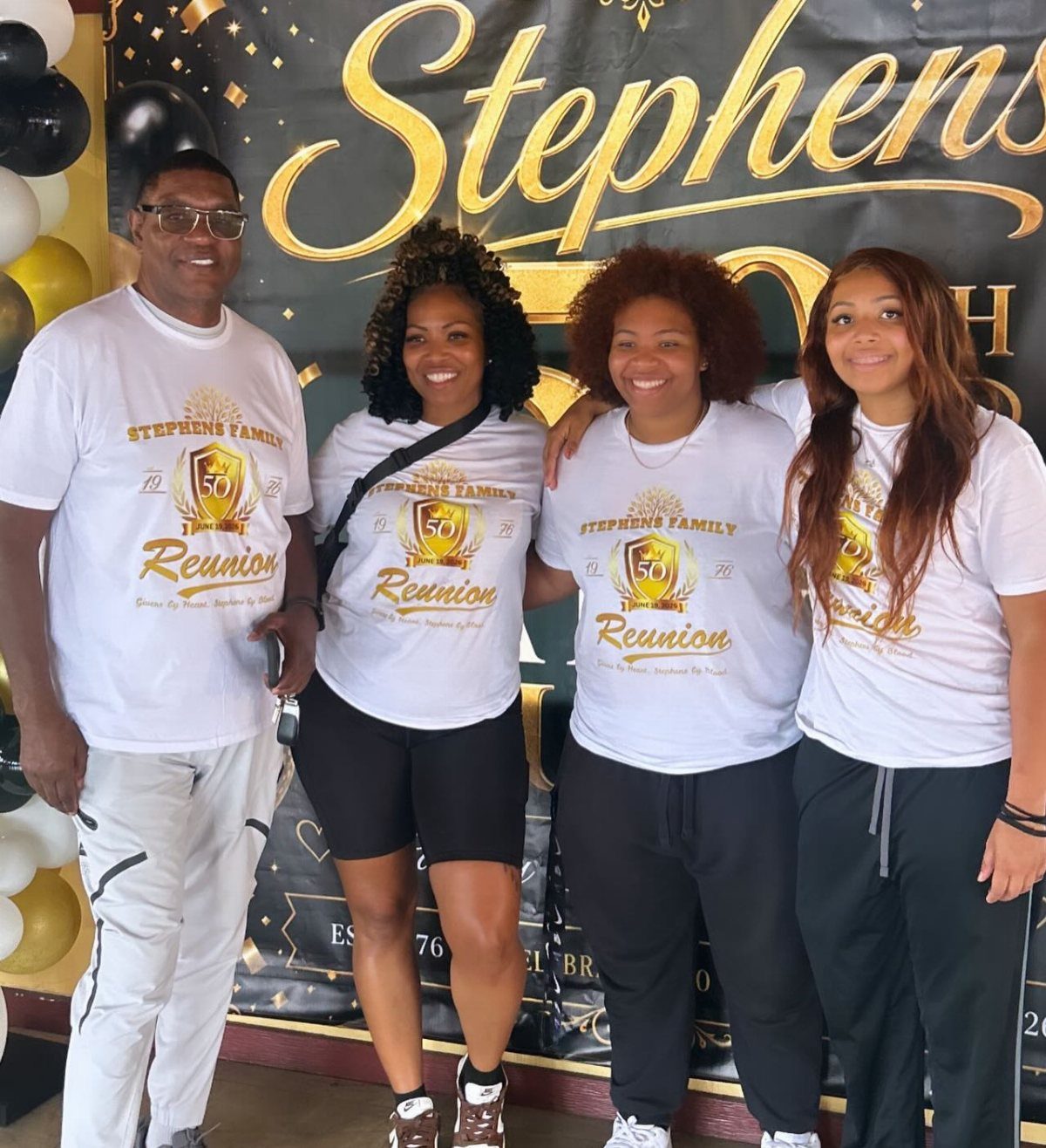 Four people wearing matching white Stephens Family Reunion t-shirts posing in front of a black backdrop.