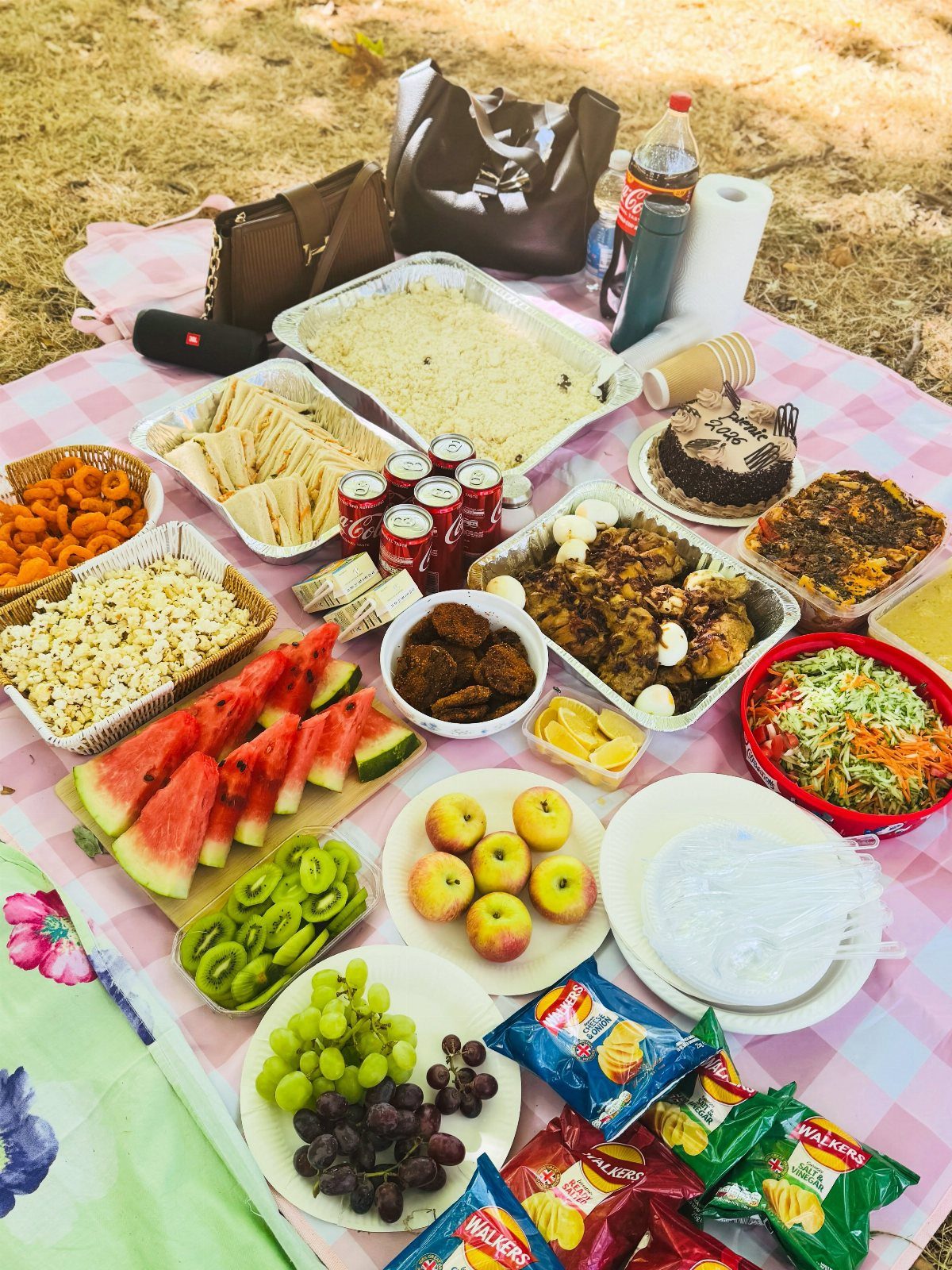 A large variety of picnic foods spread across a checkered blanket on the grass.