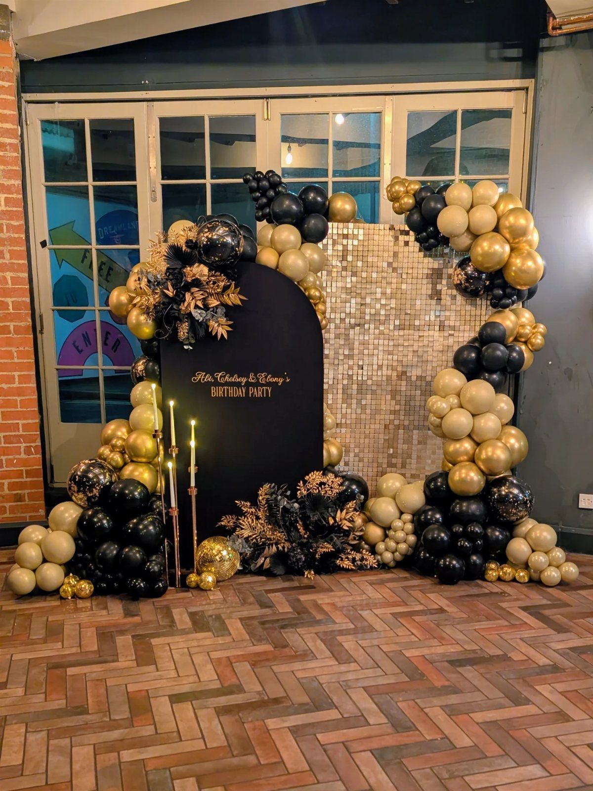 Black and gold balloon arch surrounding a black birthday party backdrop with gold accents.