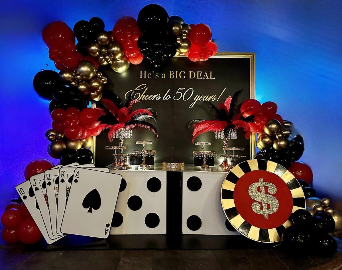 Casino-themed party decorations with balloons, large playing cards, dice, and a giant poker chip.