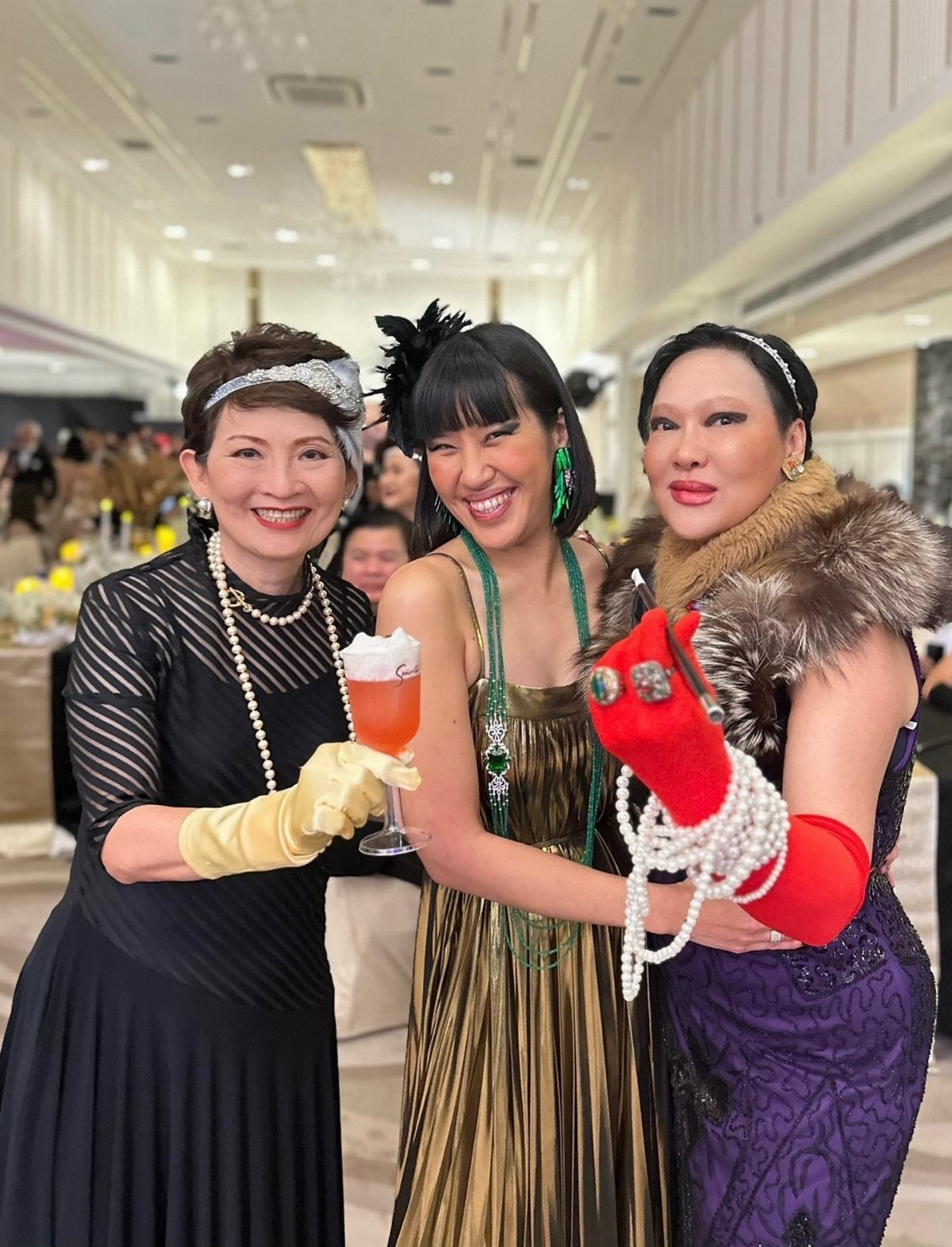 Three women dressed in glamorous 1920s vintage attire posing together at a party.