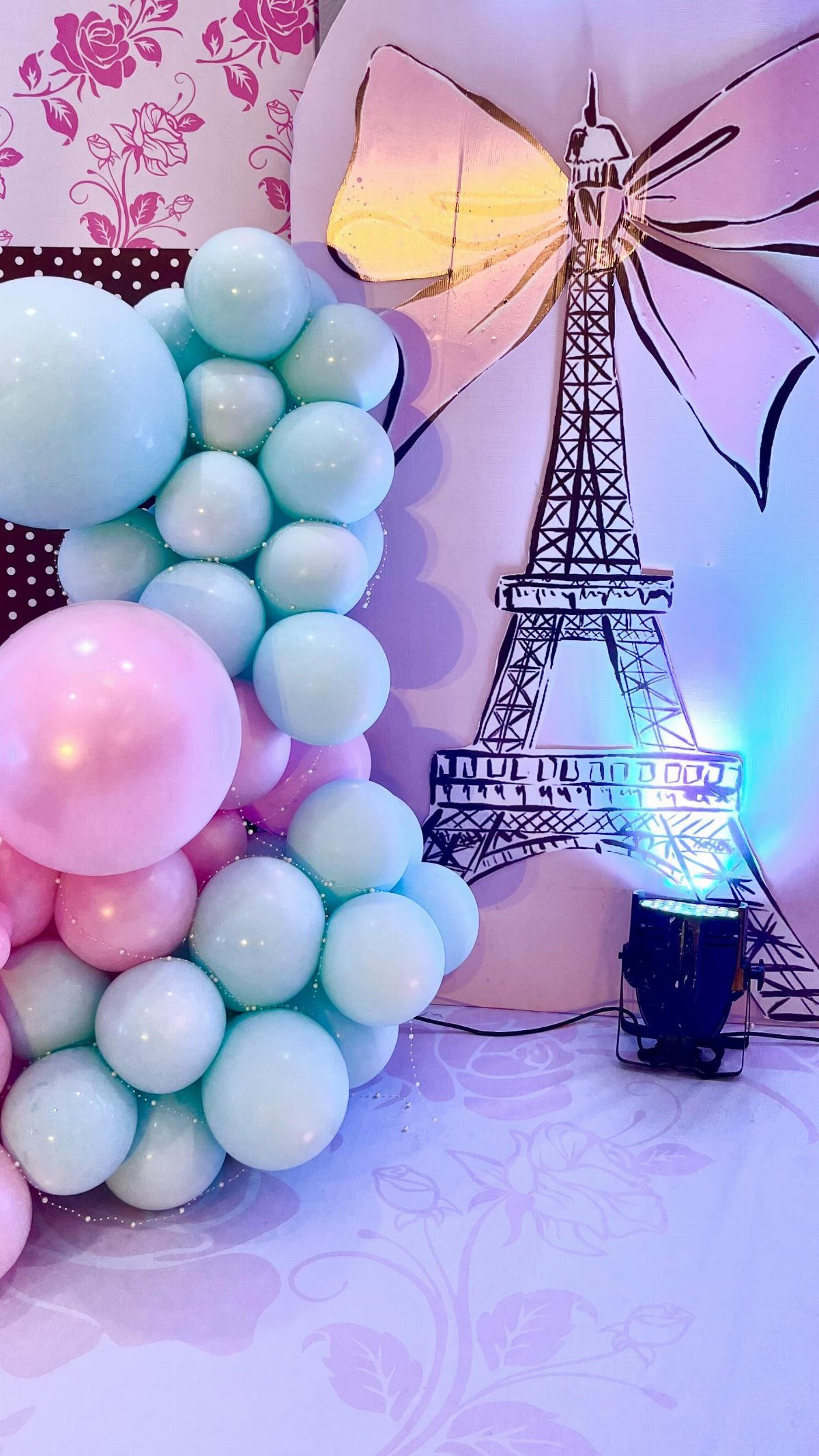 Light blue and pink balloons next to an Eiffel Tower backdrop with a gold bow.