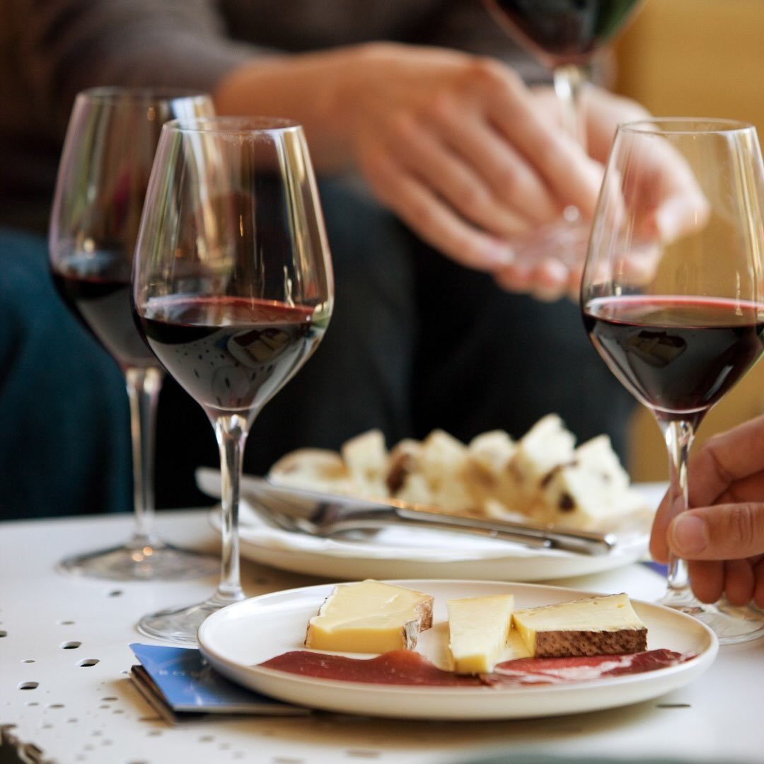 Glasses of red wine and plates of cheese and bread on a white table.