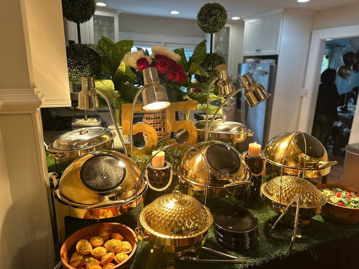 Gold chafing dishes and a large gold number 55 arranged on a buffet table.