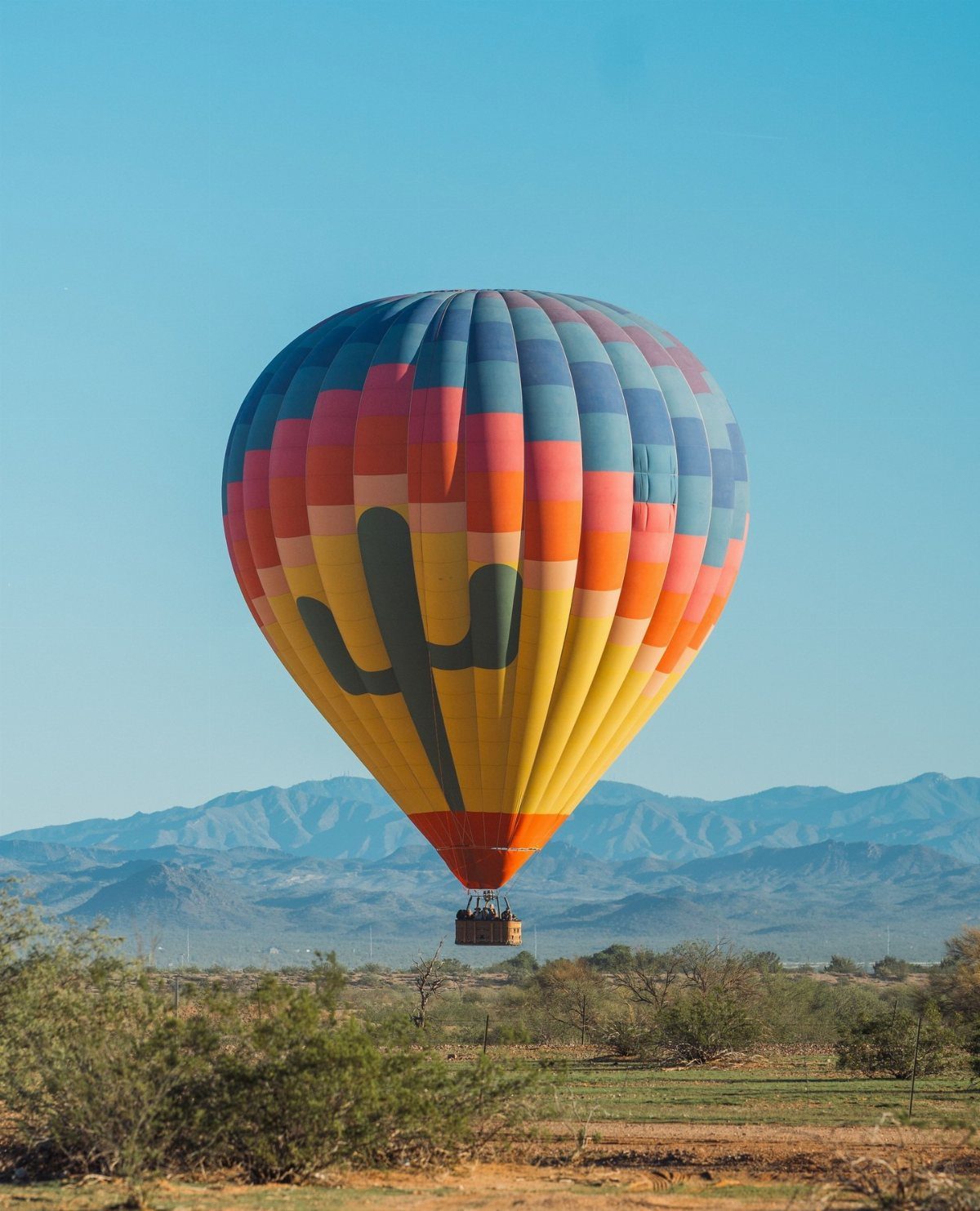 A colorful hot air balloon with a cactus design flying over a desert landscape.