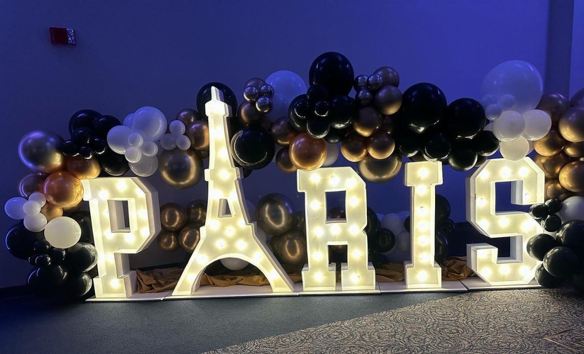 Illuminated marquee letters spelling PARIS surrounded by black, white, and gold balloons.