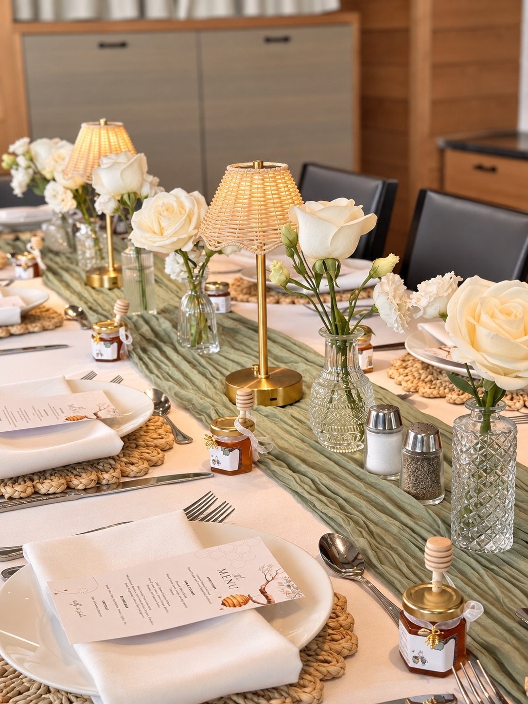 A decorated dining table featuring white roses, small lamps, and honey jars for a celebratory meal.