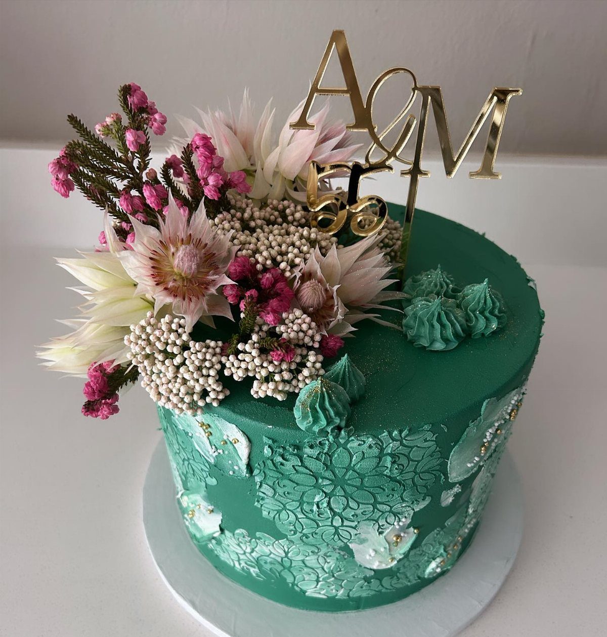 Teal frosted cake decorated with pink and white flowers and a gold 55th birthday cake topper.