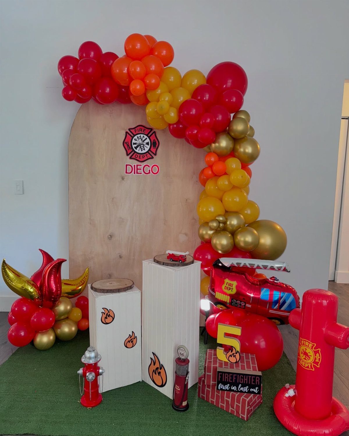 Firefighter themed birthday party decorations with red balloons, a wooden backdrop, and fire hydrant props.