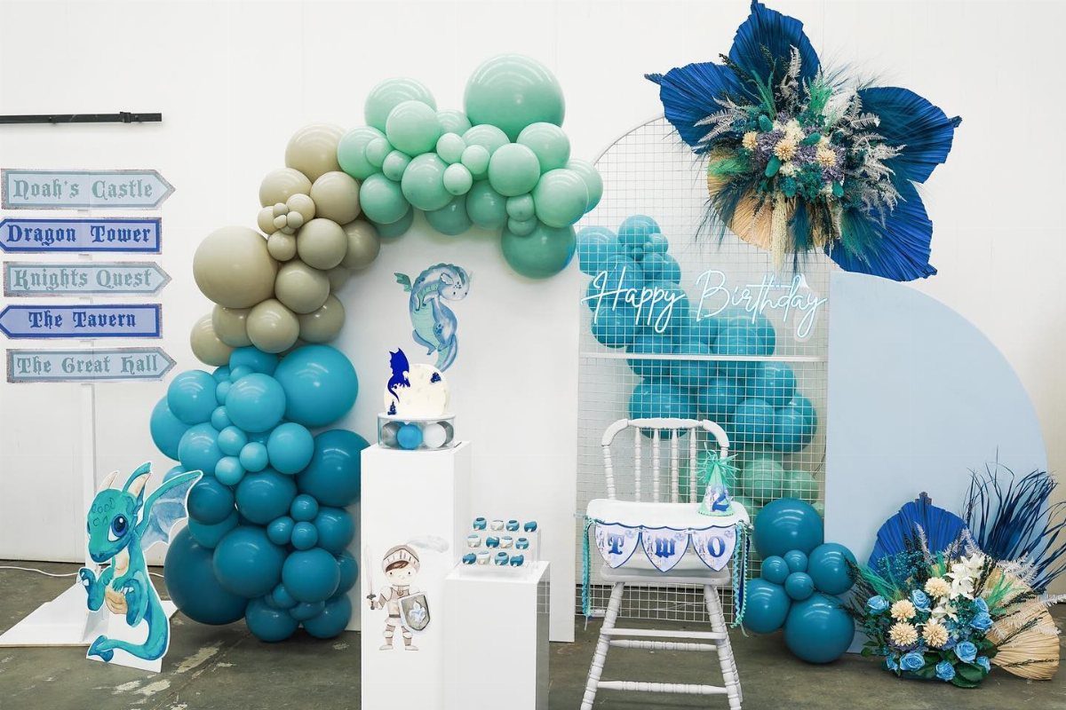 Blue balloon arch with dragon and knight cutouts for a themed birthday party setup.