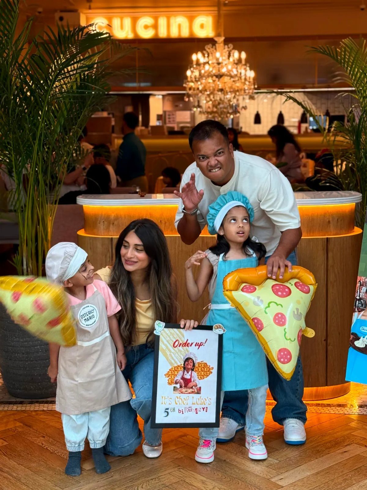 A family posing with children wearing chef hats and holding large plush pizza slices.
