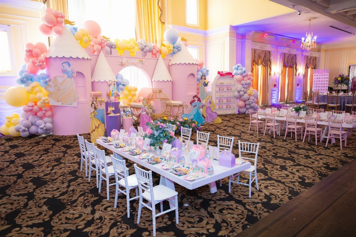 A pink castle backdrop with pastel balloons and a decorated long table in a ballroom.
