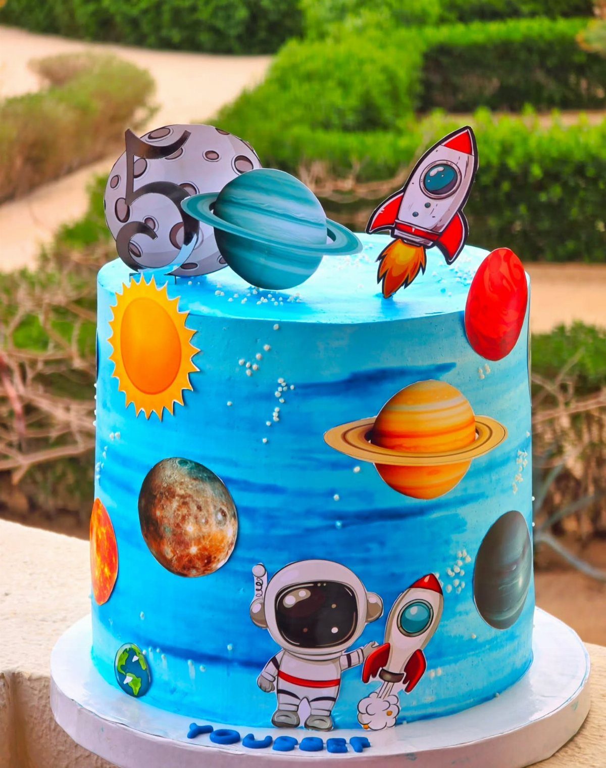 A blue space-themed birthday cake decorated with astronauts, rockets, and various colorful planets.