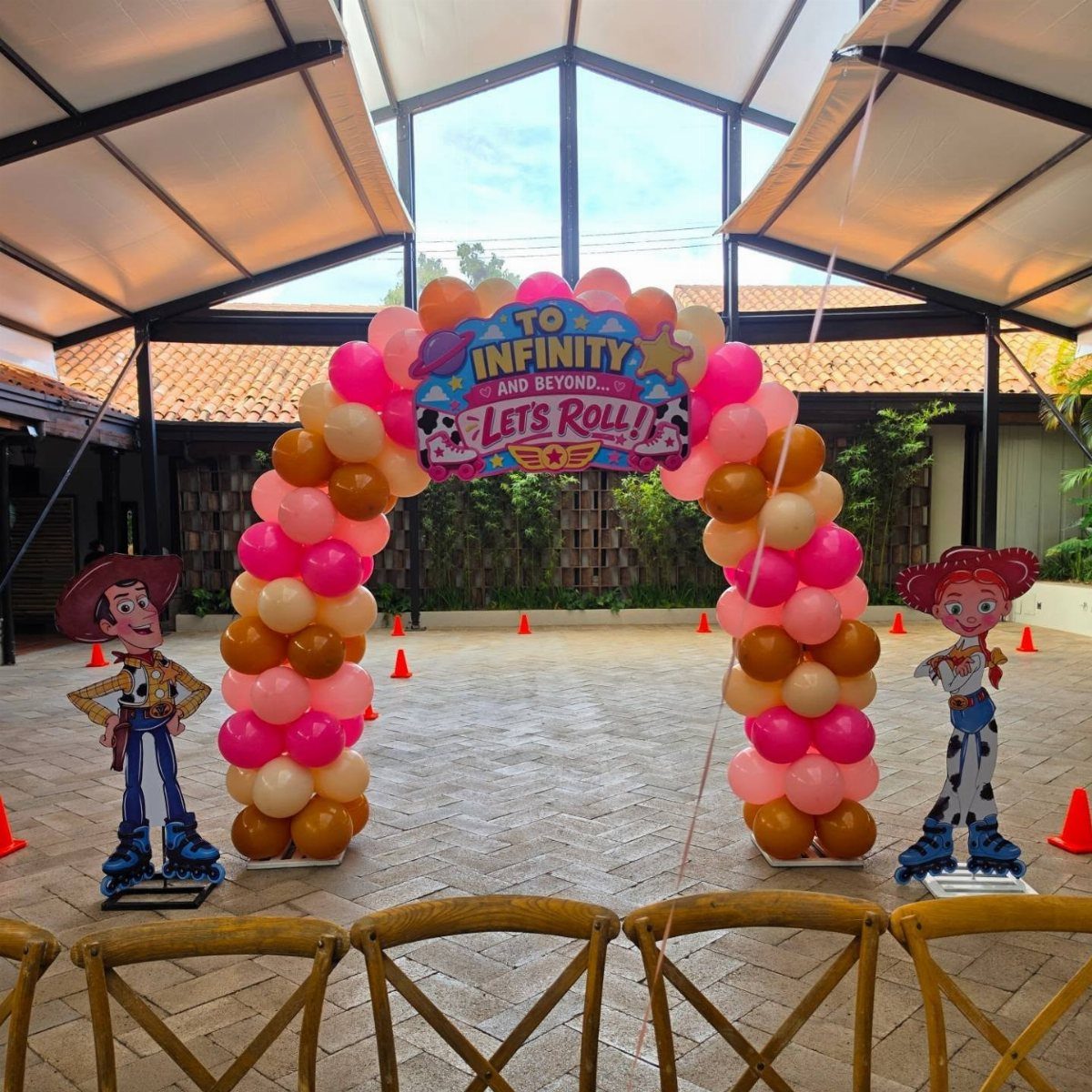 Balloon arch with Toy Story character cutouts standing on a paved patio area.