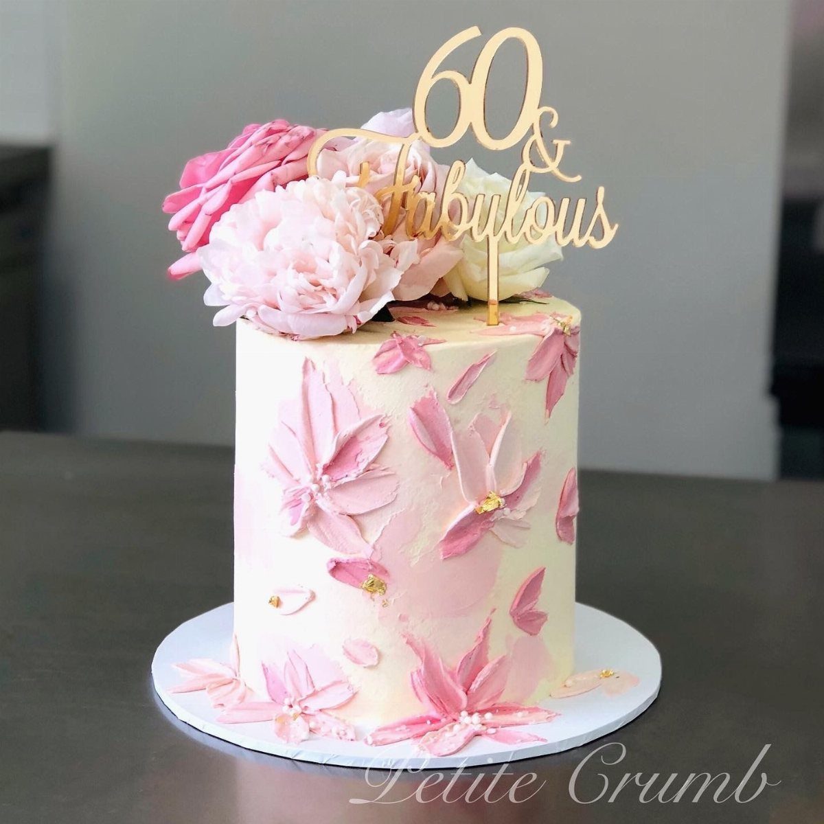 Cream-colored cake with pink floral buttercream decorations and a gold 60 & Fabulous topper.