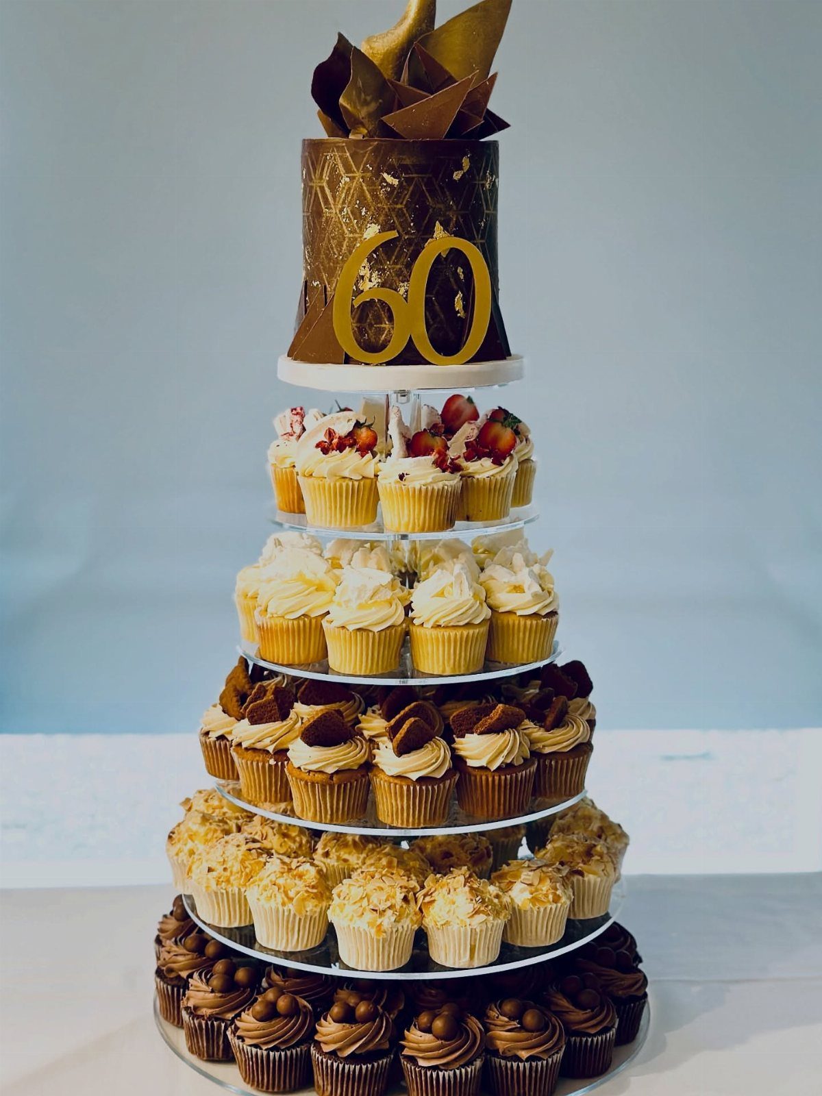 A tiered cupcake tower topped with a gold number 60 cake and various frosted cupcakes.