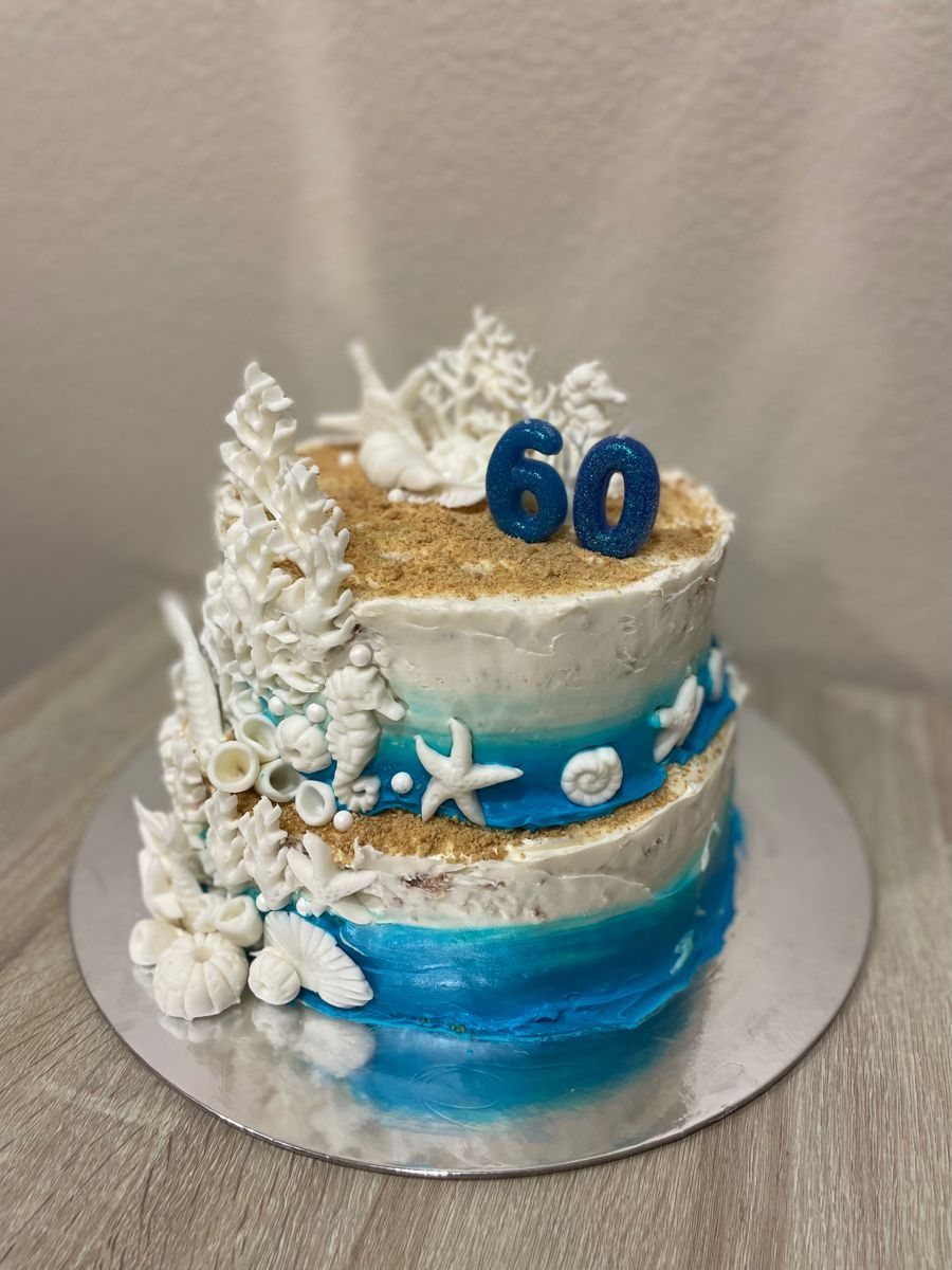 Two-tier blue ombré cake decorated with white seashells, coral, and blue number 60 topper.