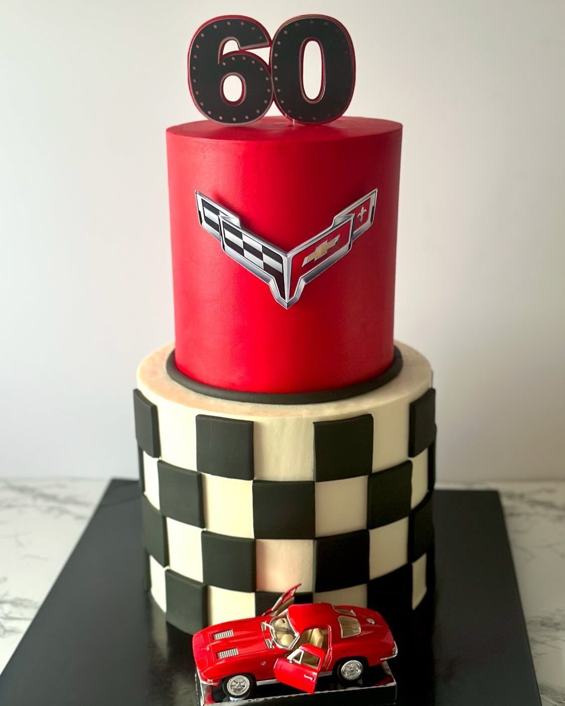 Two-tier red and checkered cake with a Chevrolet emblem, a red toy car, and a 60 topper.