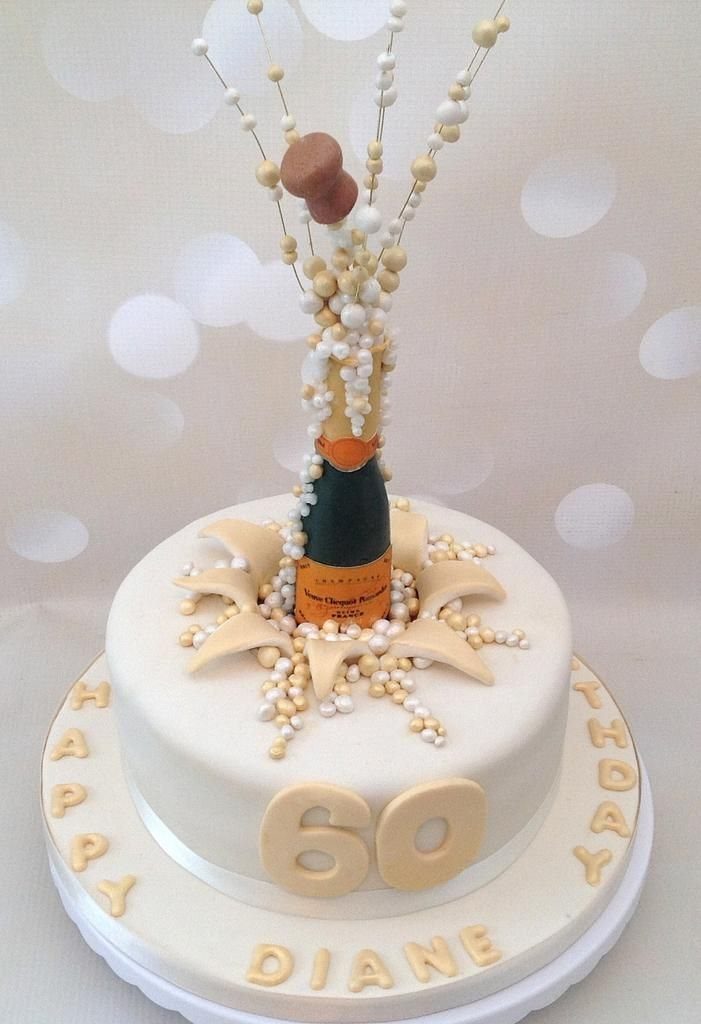 White cake featuring an exploding champagne bottle decoration and gold sixty birthday lettering.