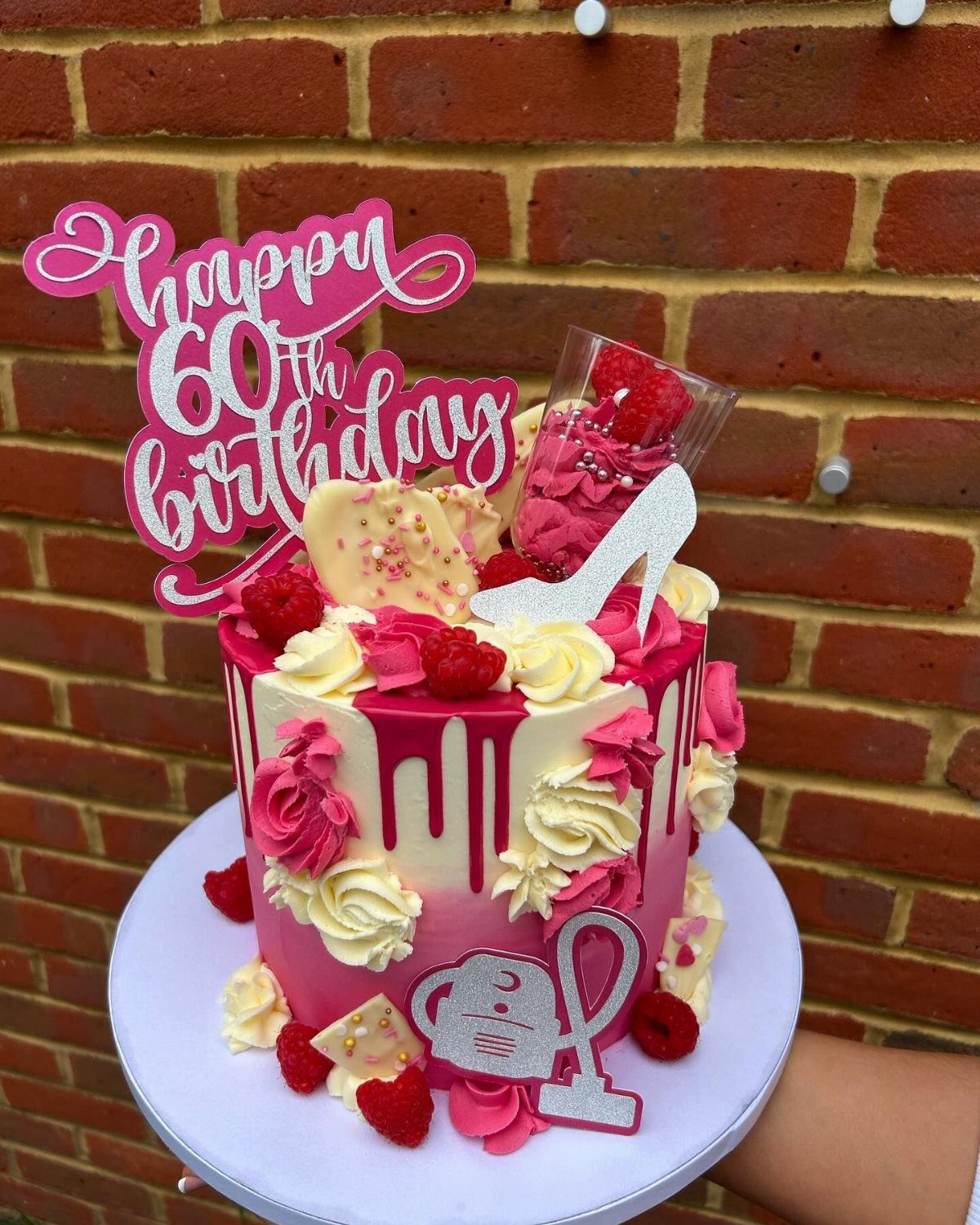 Pink ombre birthday cake with raspberries, frosting swirls, and a happy 60th birthday topper.
