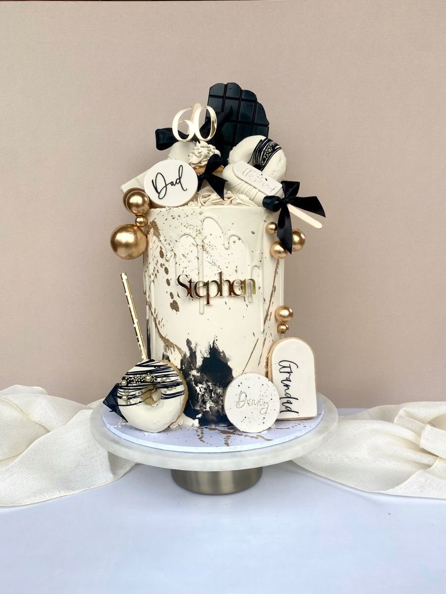 A white and black decorated cake with gold accents, featuring a sixty topper and nameplate.