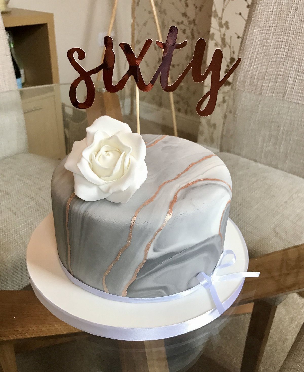 Marble effect cake with a white rose and a sixty topper on a white stand.