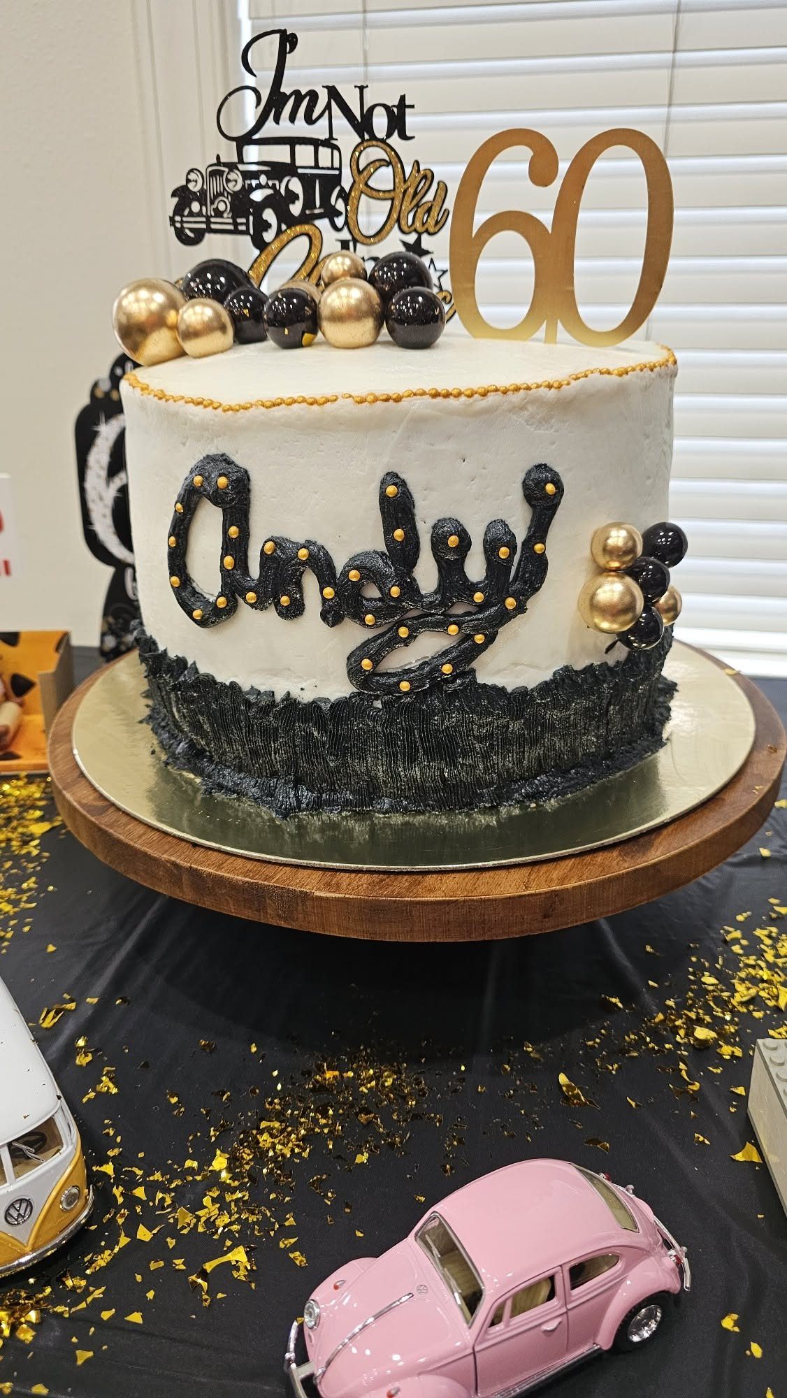 A white and black birthday cake with gold number sixty and name Andy toppers.