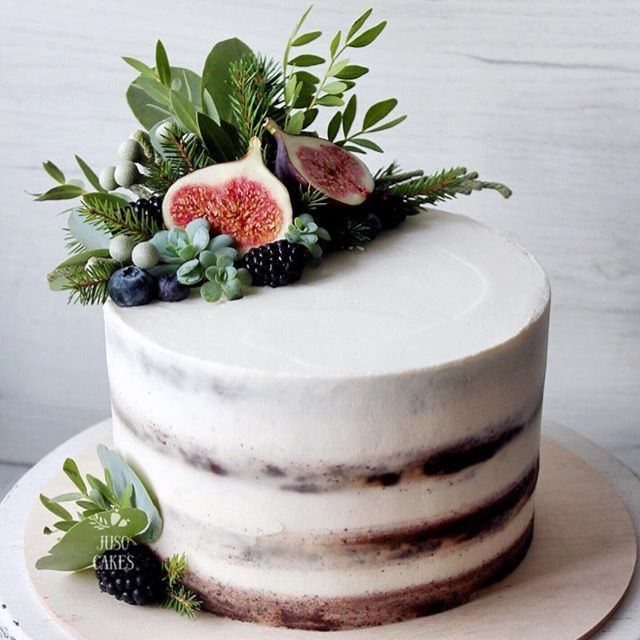 Naked cake topped with fresh figs, blackberries, blueberries, and green foliage on a wooden board.