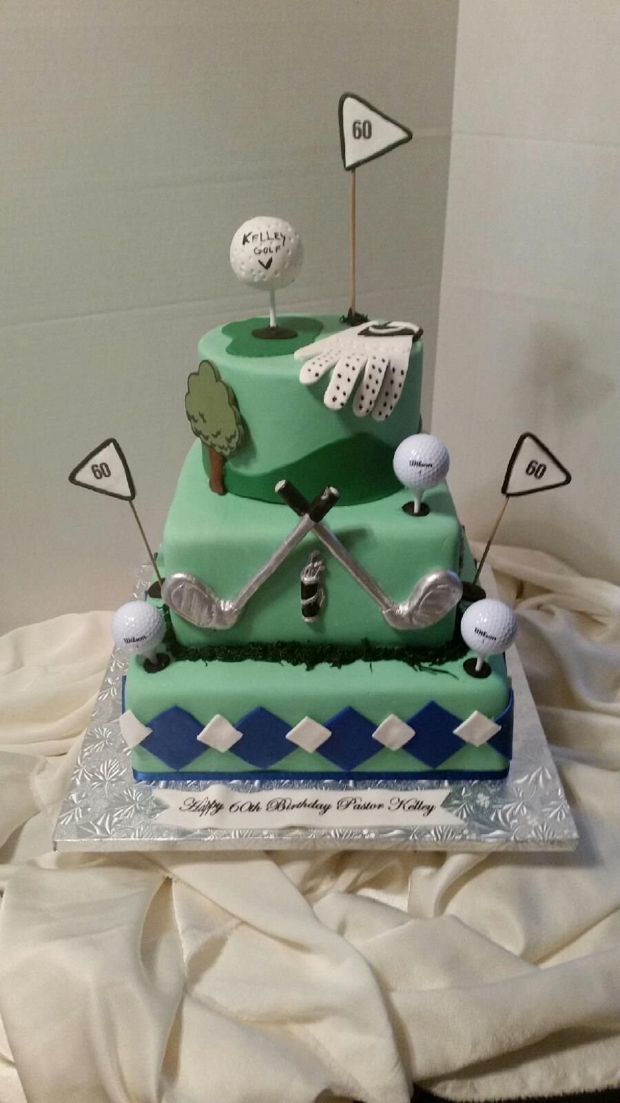 Two-tier green golf-themed birthday cake decorated with edible golf balls, clubs, and flags.