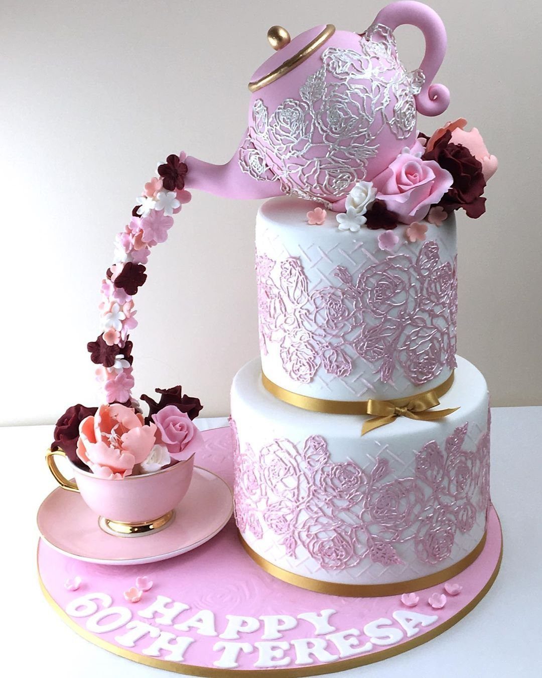 Two-tiered pink floral cake featuring a teapot pouring flowers into a teacup.