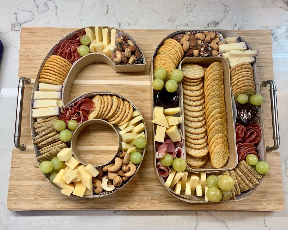 Charcuterie trays shaped like the number sixty filled with cheese, crackers, meats, and grapes.