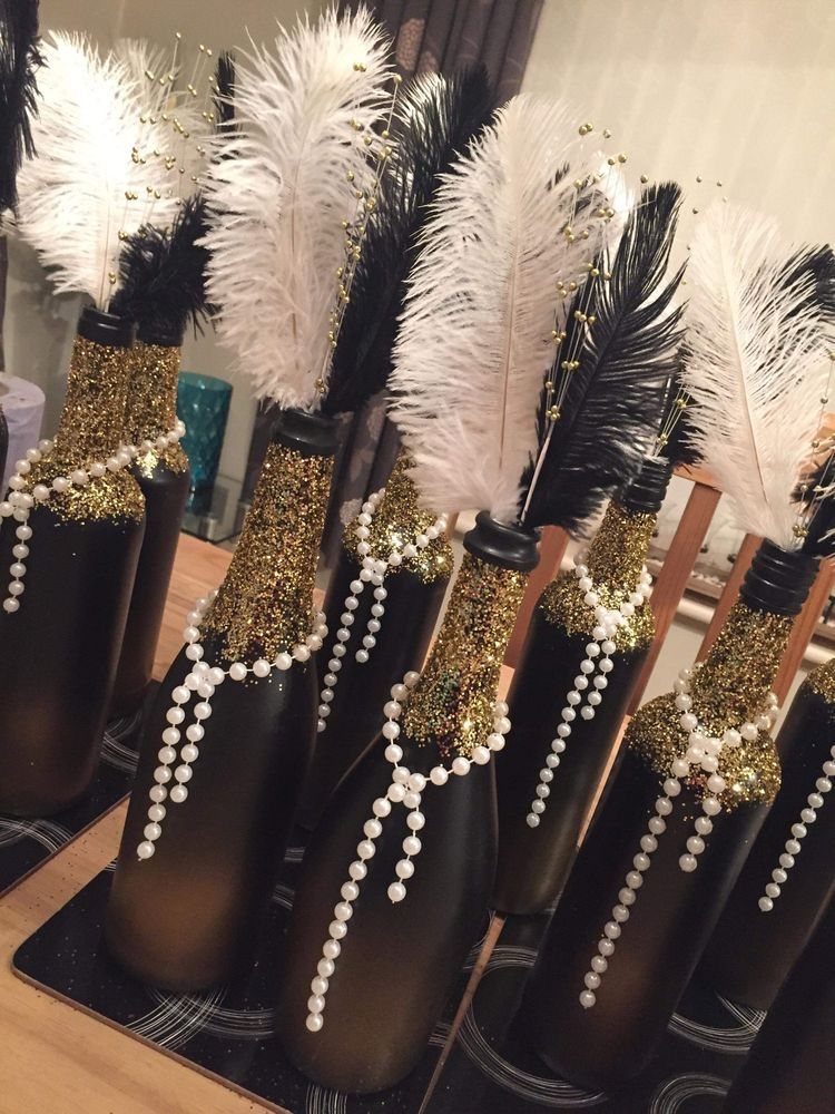 Black decorative bottles adorned with gold glitter, white pearls, and large black and white feathers.