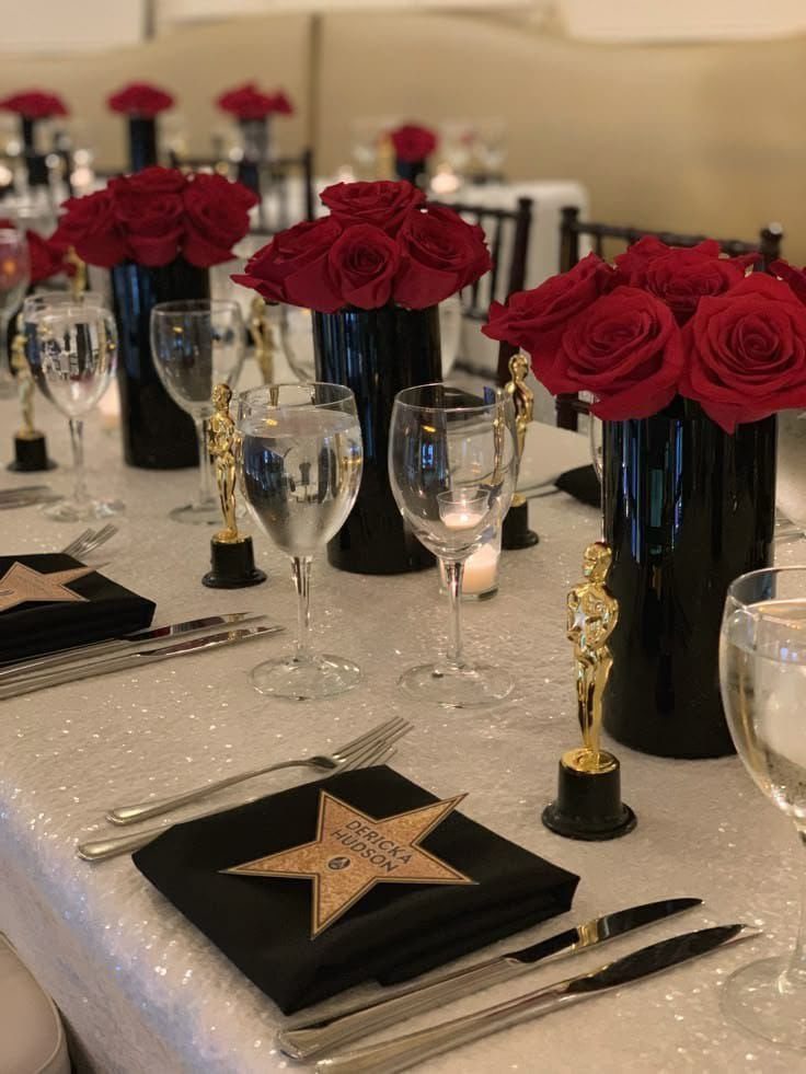 Formal table setting with red roses, gold trophies, and star-patterned black napkins on sequins.