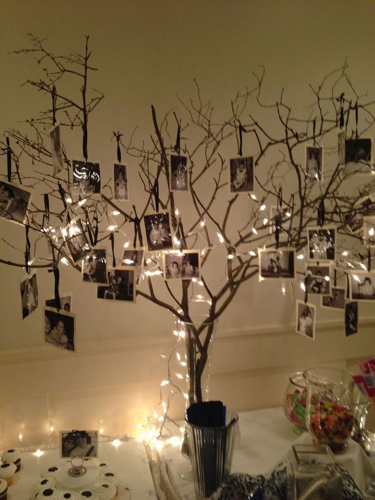 A decorative branch tree adorned with hanging black and white photographs and glowing fairy lights.