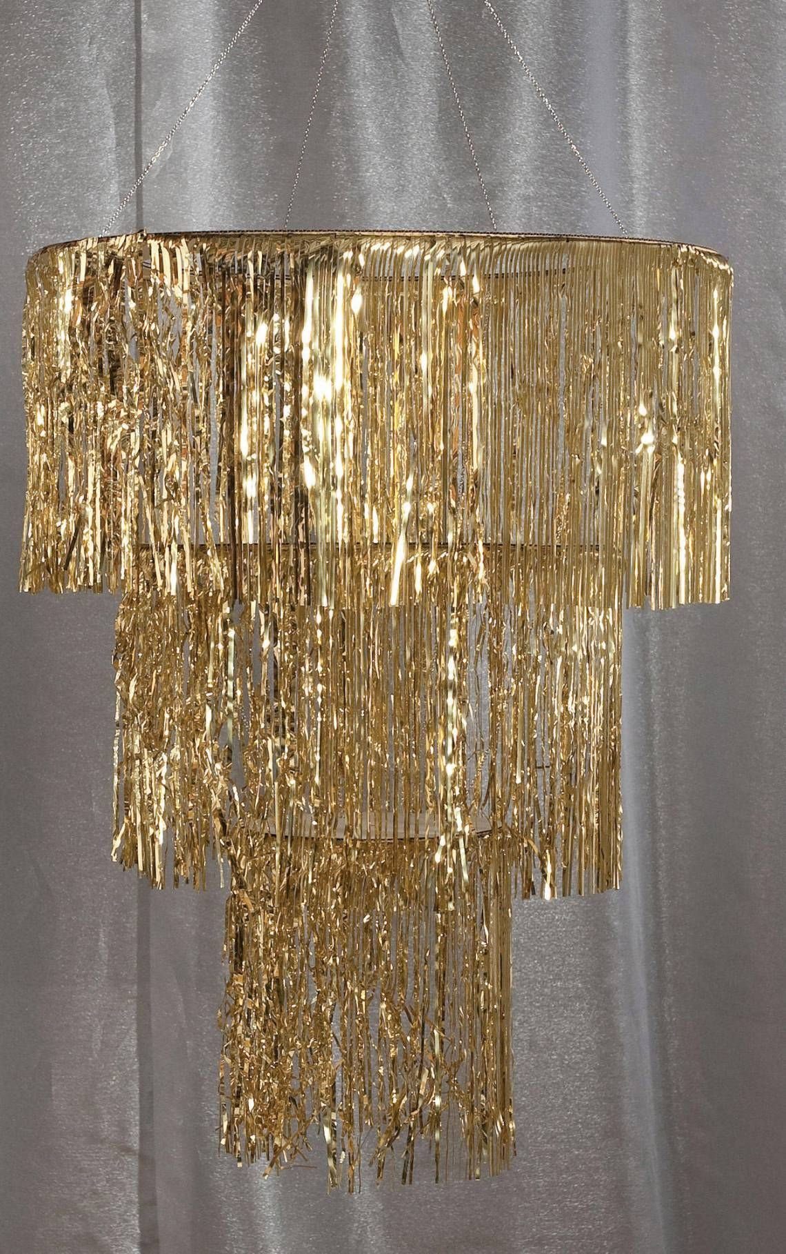 Tiered gold metallic fringe chandelier hanging against a white fabric backdrop.