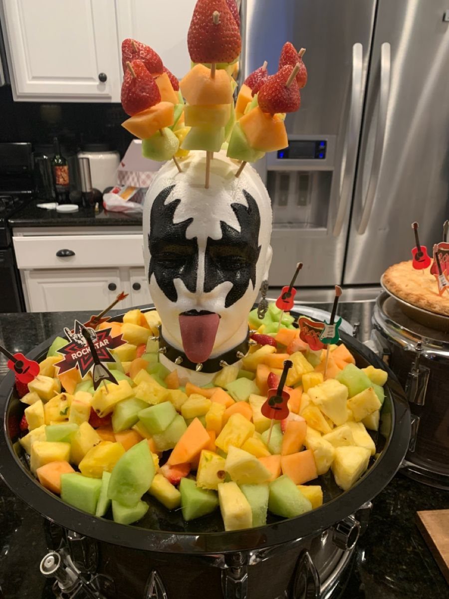 Fruit platter featuring a KISS-style face mask decorated with fruit skewers on a drum.