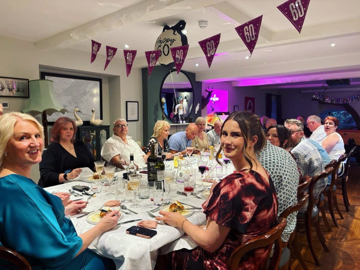 A group of people dining together at a long table decorated with purple 60th birthday bunting.