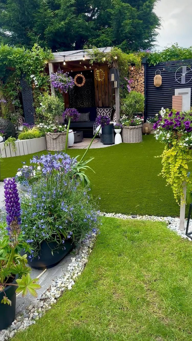 Lush garden setting with purple flowers, green turf, and a decorated wooden pergola.