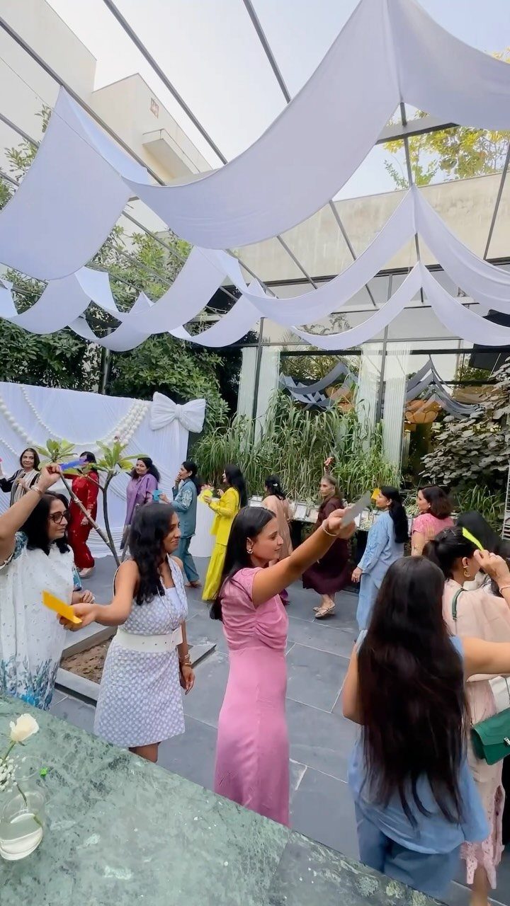 Women in colorful dresses holding yellow cards while playing a game outdoors under white fabric.