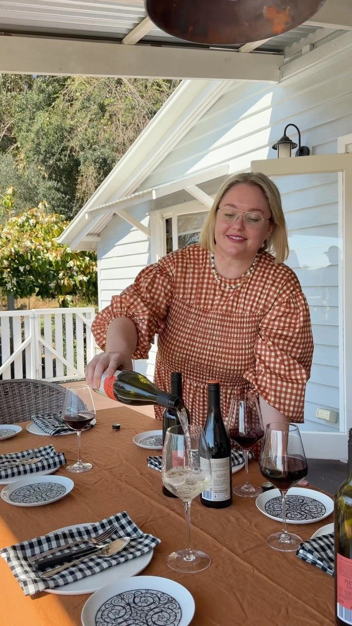 A woman pouring white wine into a glass at a set outdoor dining table.