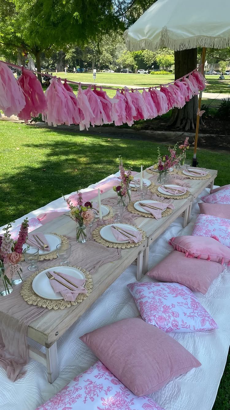 A low wooden table set with pink decor and pillows for an outdoor picnic.