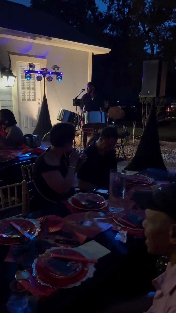 Musician playing percussion instruments for guests seated at an outdoor dinner table at night.
