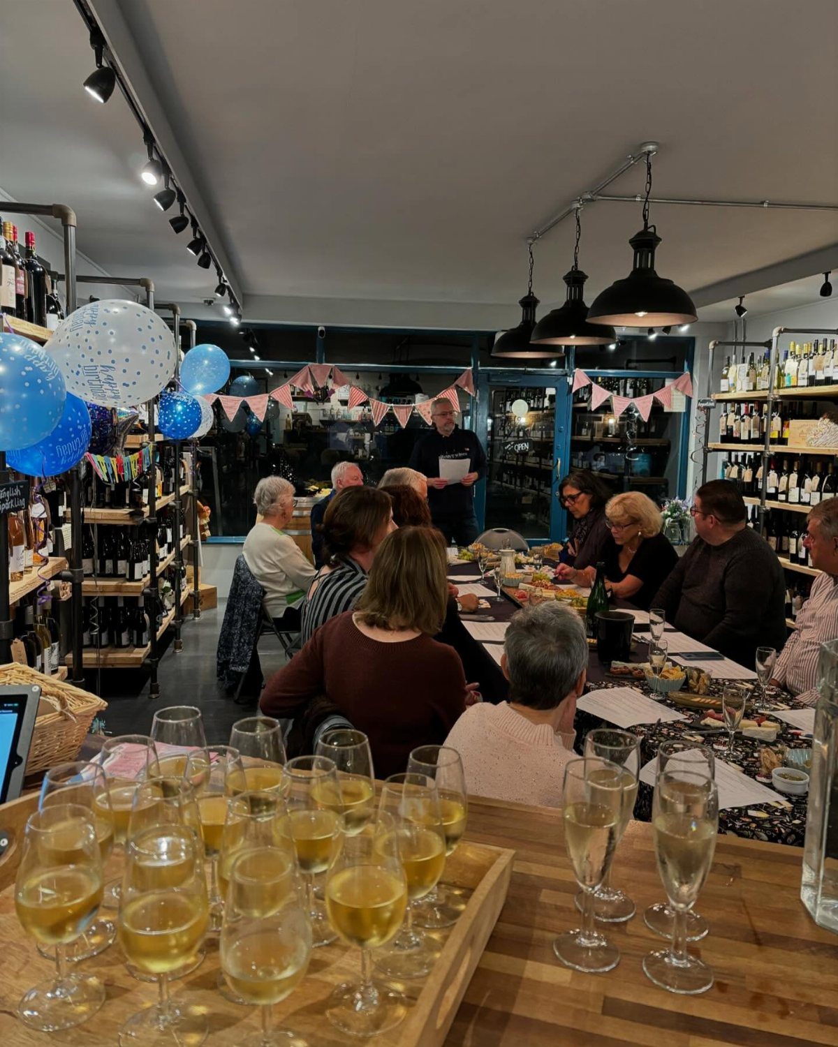 People seated at a long table for a wine tasting event surrounded by wine bottles.
