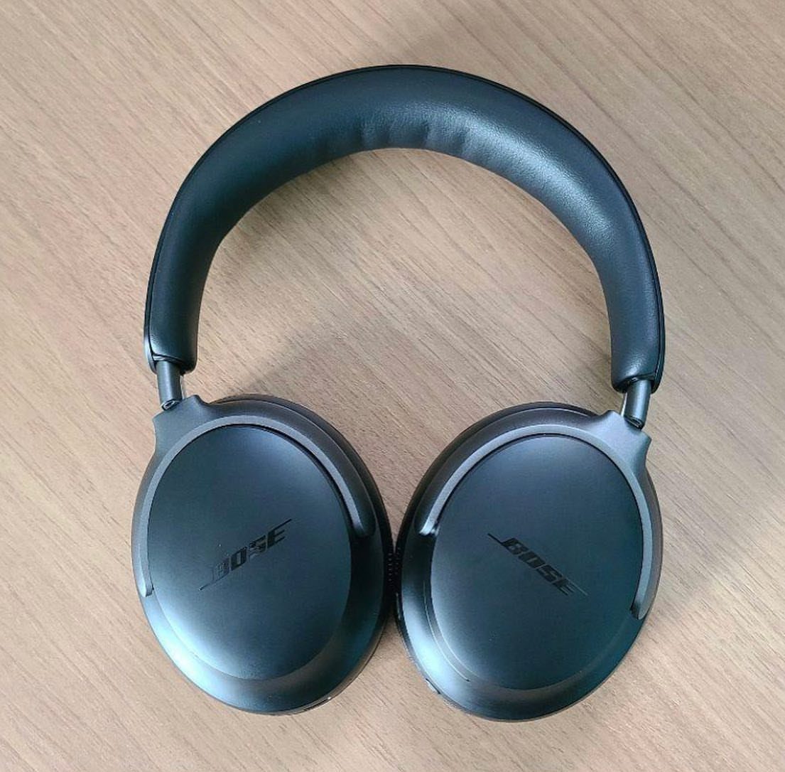 Black Bose noise-cancelling headphones resting on a light wooden tabletop surface.