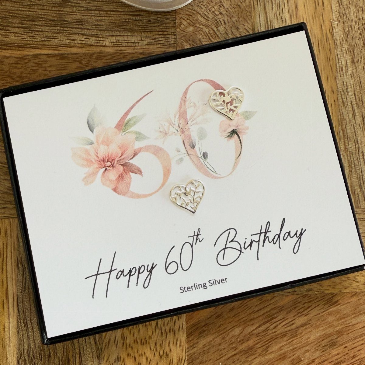 Silver heart-shaped filigree earrings resting on a white birthday greeting card.